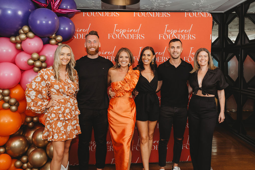 Six Inspired Founders guests posing together against the red backdrop beside the balloon arch